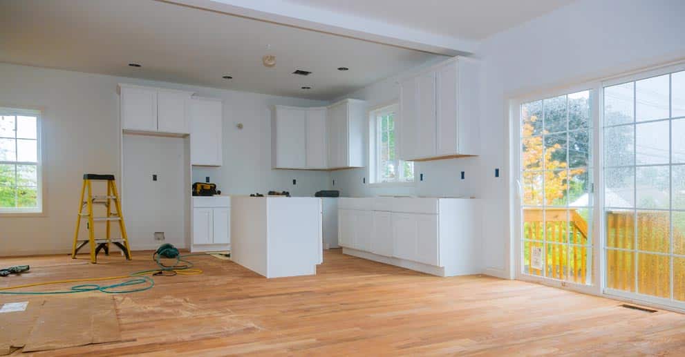 A kitchen being remodeled with white cabinets and hardwood floors
